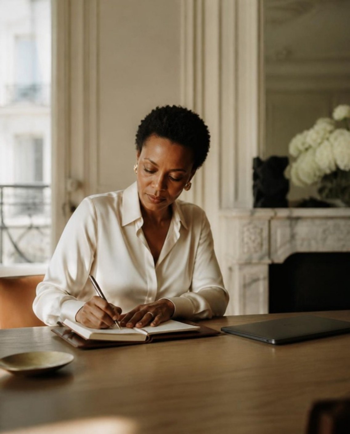 A woman founder in an ivory silk shirt writing in a notebook at her desk, morning light